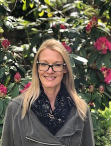 Pia Smith, psychotherapist, standing outdoors in front of a flowering shrub